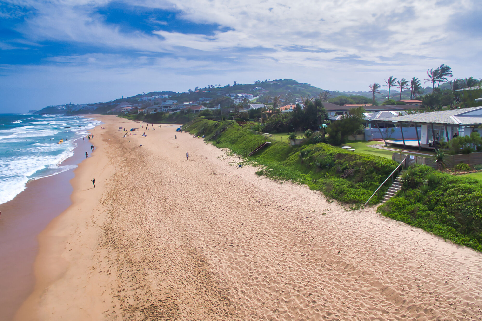 An aerial view from the right side of the beach, with partial view of the ocean, beach, skyline, and the holiday home.
