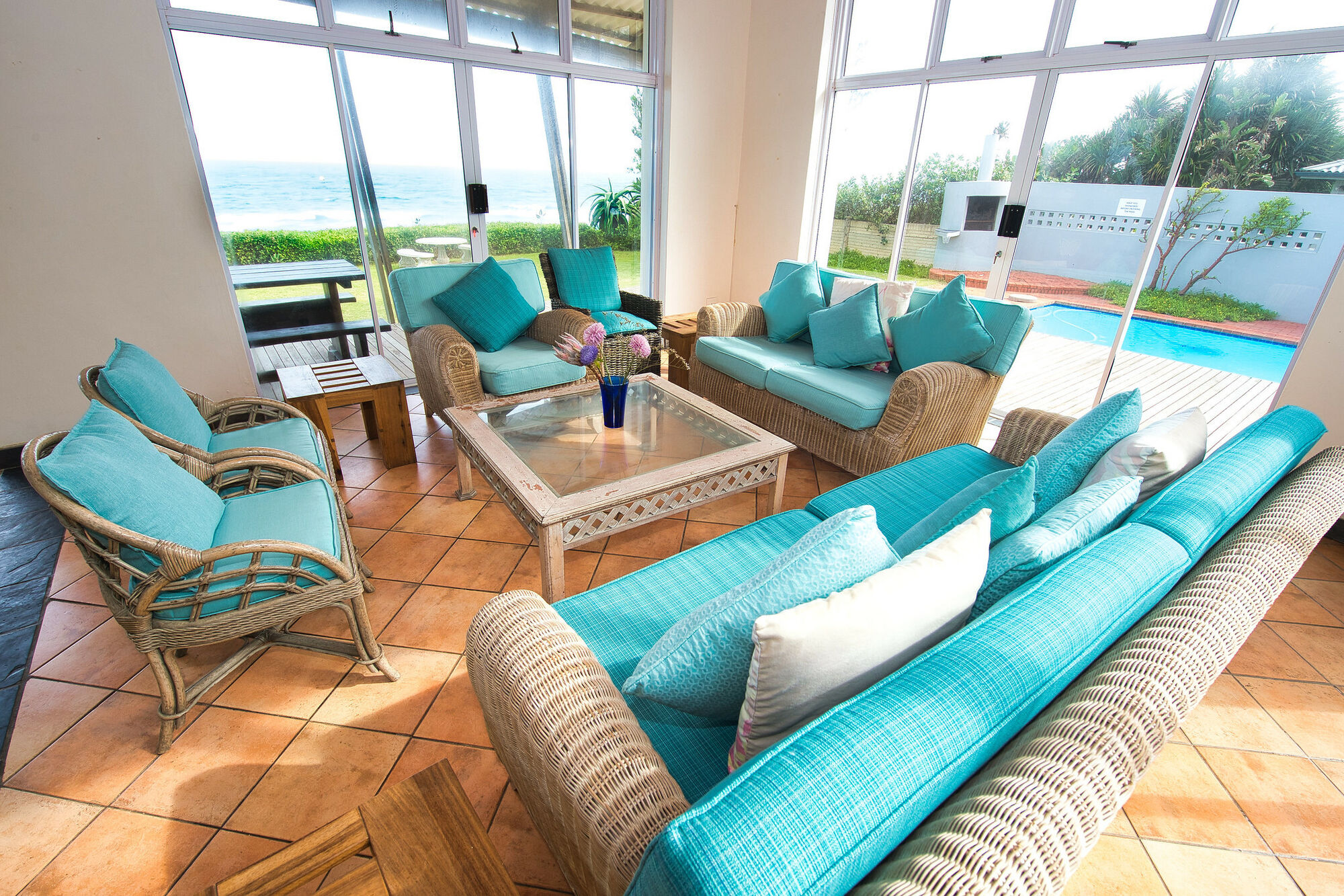 Rascal’s Rest - lounge area, wooden and teal cushioned furniture. Looking out onto the ocean