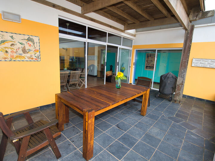 Outside deck area. Open roof, yellow walls, wooden furniture, dark grey tiling.
